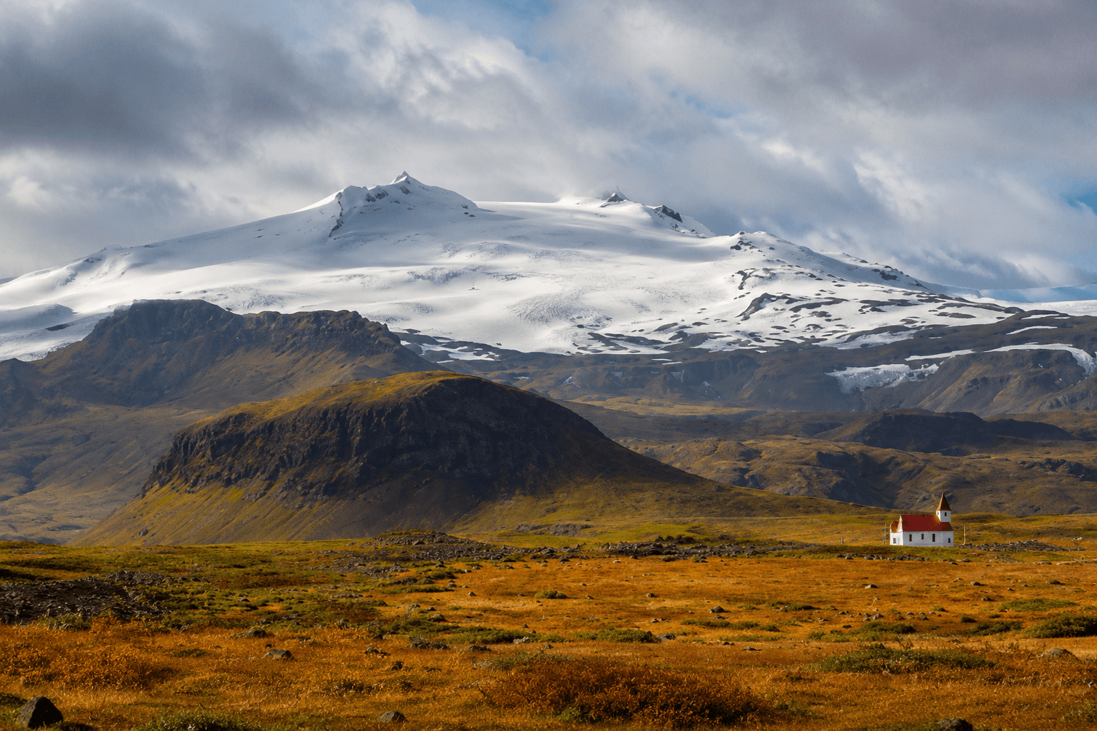 Icelandic mountain with snow surrounded by dry yellow grass and cloudy weather