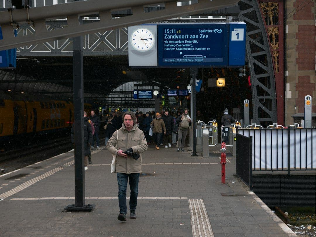 A traveller walking along a platform under the historic roof of Amsterdam Centraal station.