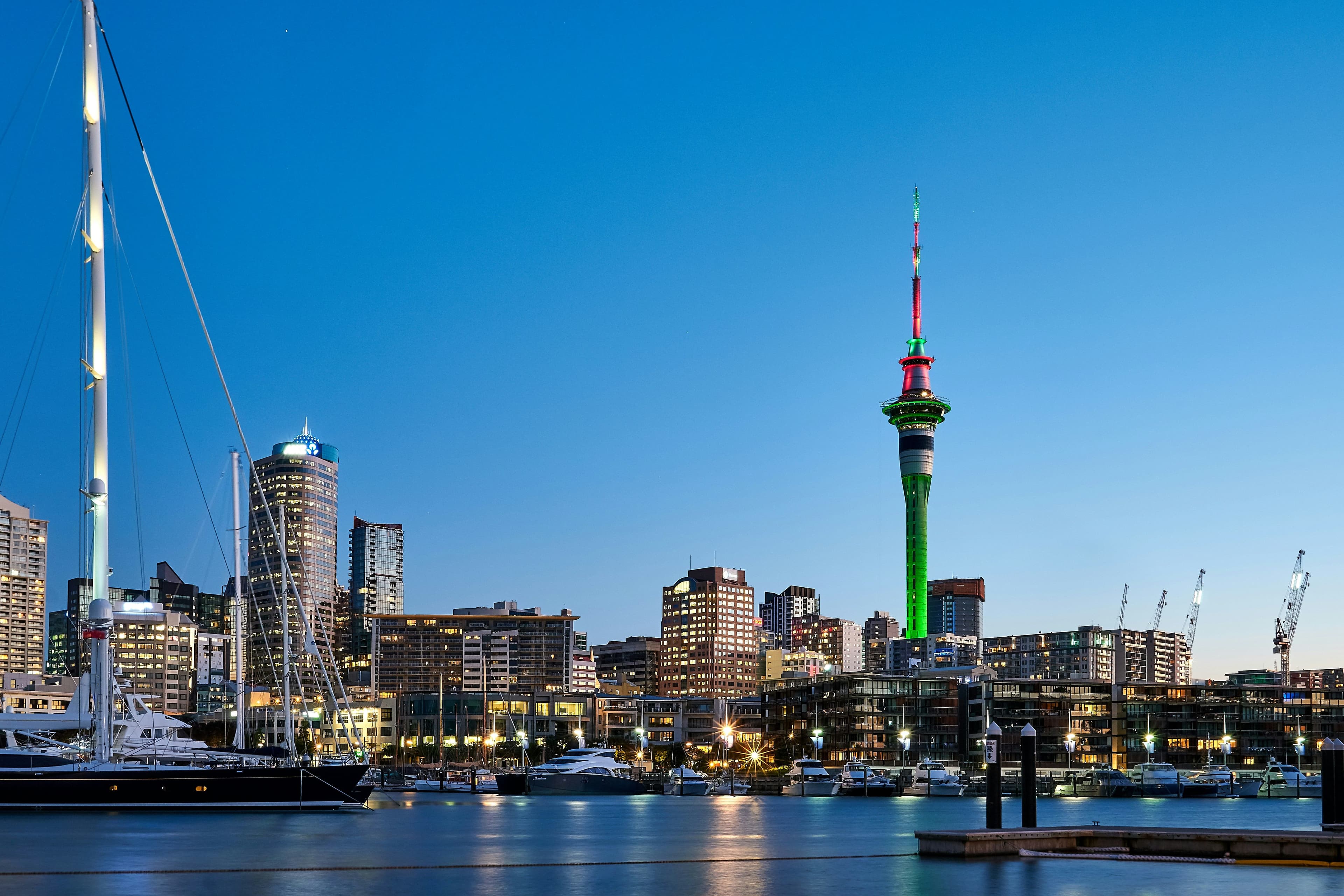 Auckland harbor with sailing boats and water and skyline at night with a blue sky