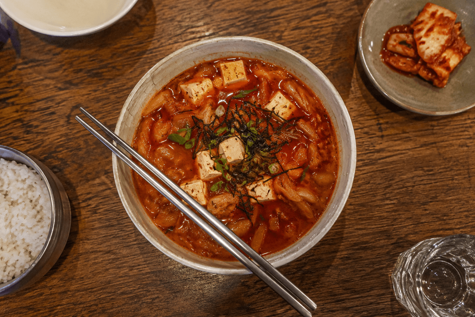 A plate with orange Kimchi with tofu and chopping sticks on a wooden table