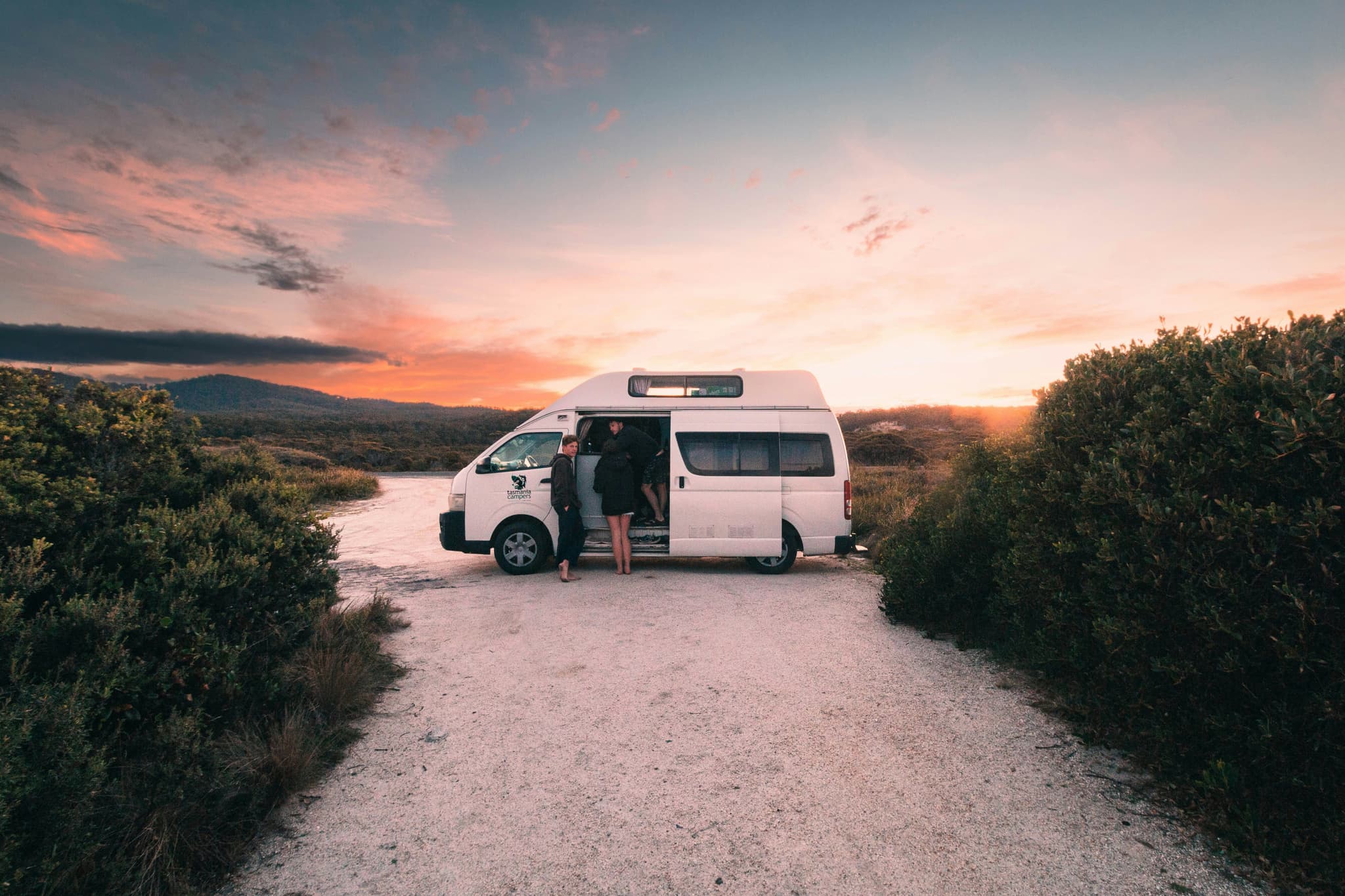 A campervan parked in a sandy area during sunset