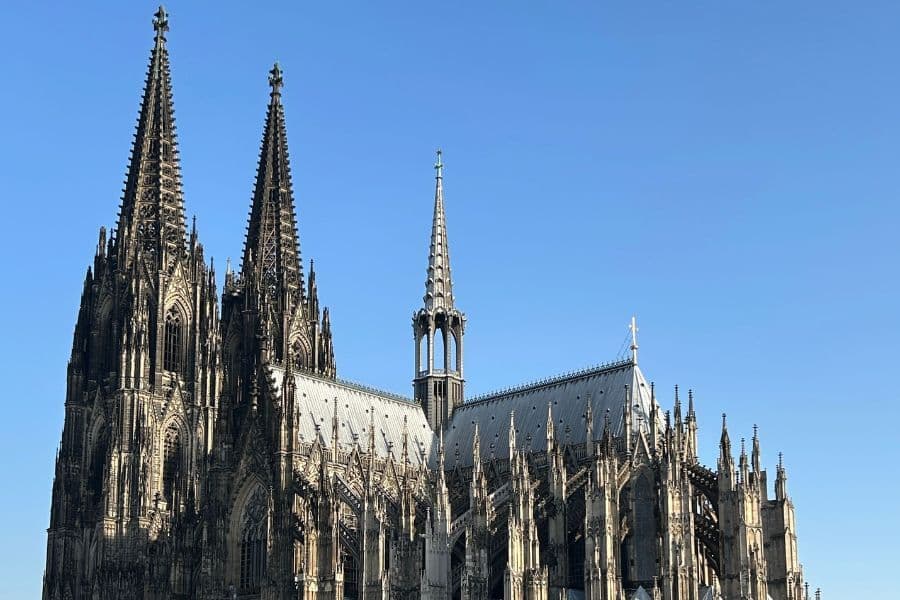 A bright photo of the massive Gothic architecture of Cologne Cathedral against a clear blue sky.