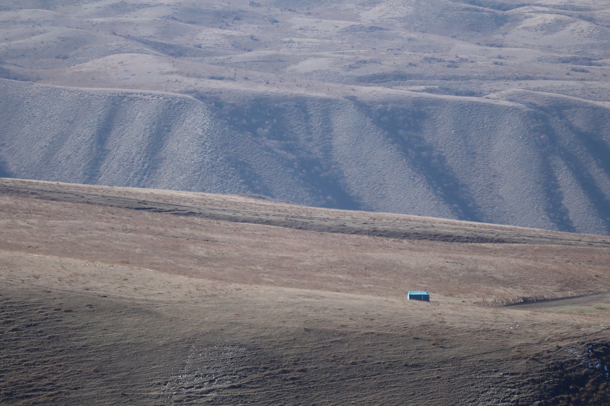 A car on a dirt track past a shepherd's shelter in the Kyrgyz mountains
